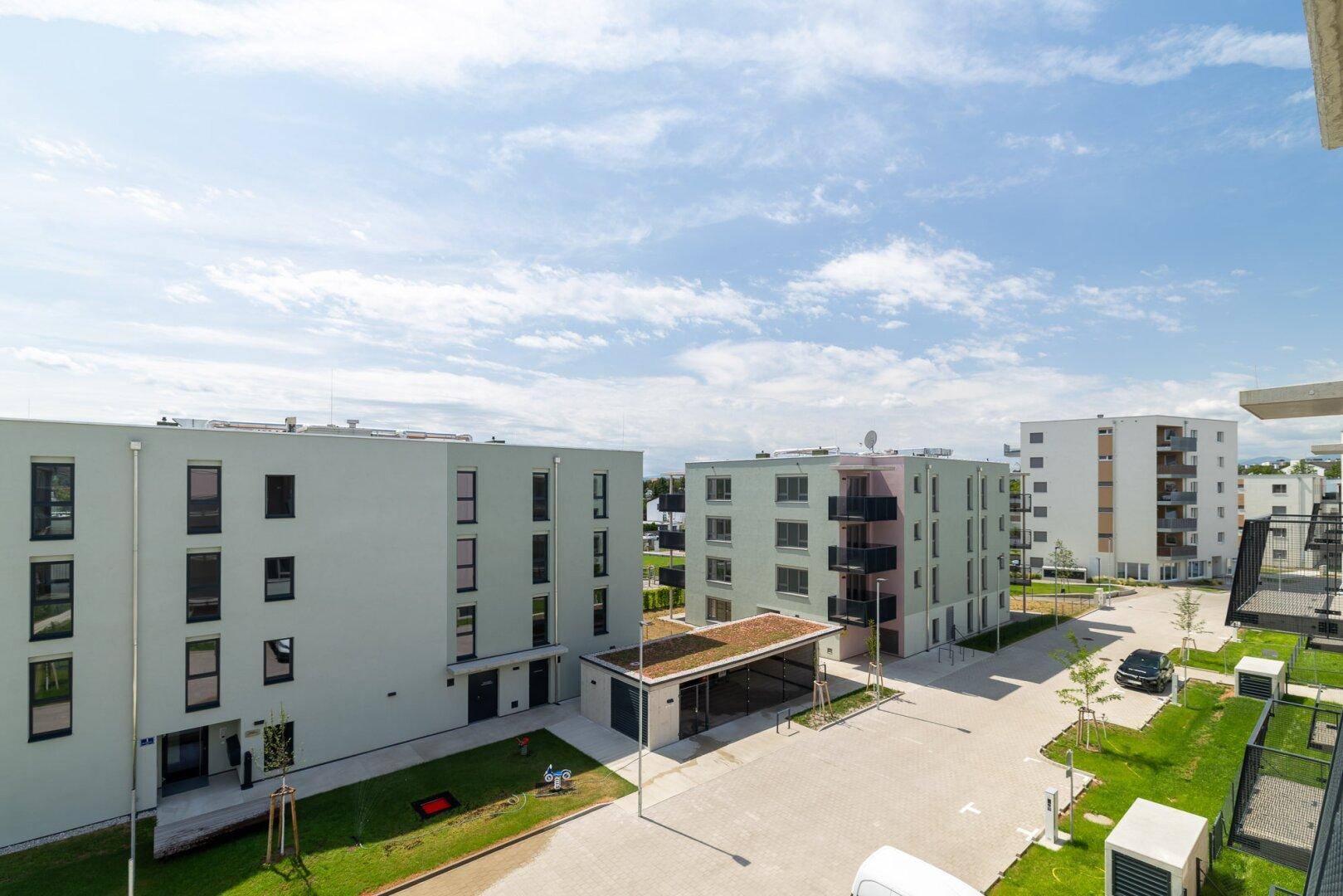 Weitläufige Ansicht einer modernen Wohnsiedlung mit mehreren Gebäuden, Grünflächen und Parkplätzen.