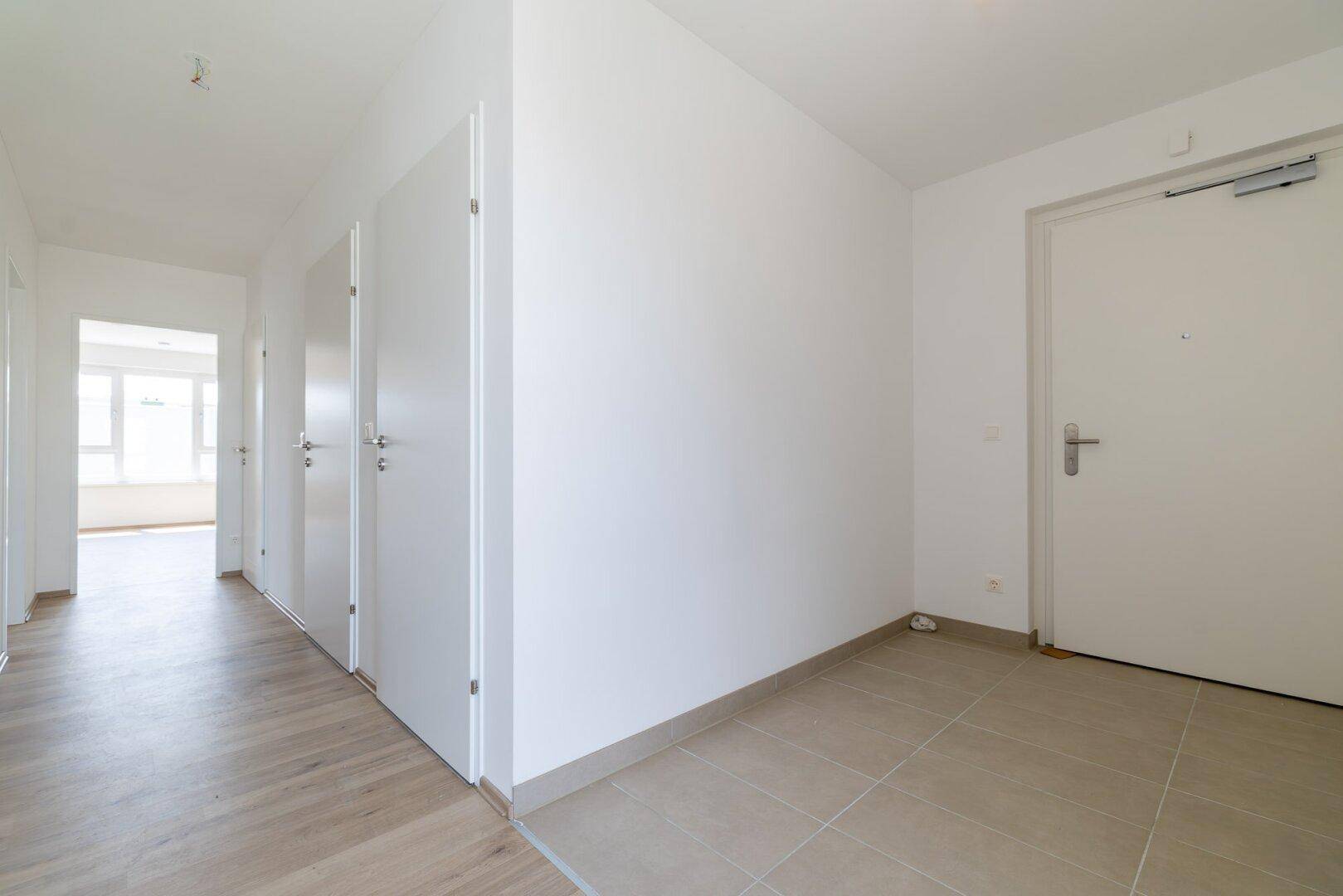 Heller Flur mit einer Kombination aus Laminat- und Fliesenboden, der zu verschiedenen Räumen führt.