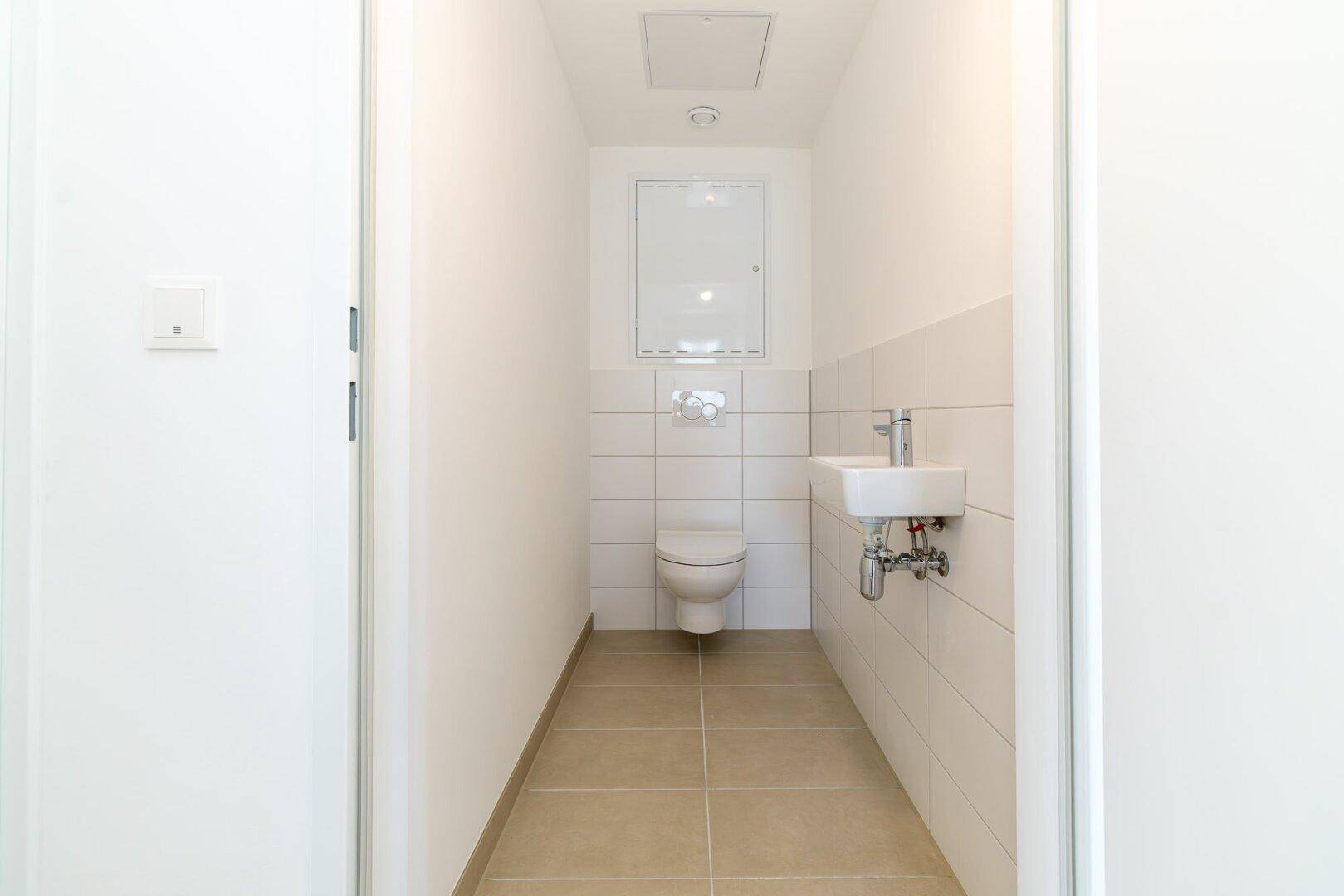 Modernes Gäste-WC mit wandhängender Toilette, kleinem Waschbecken und hellen Fliesen.