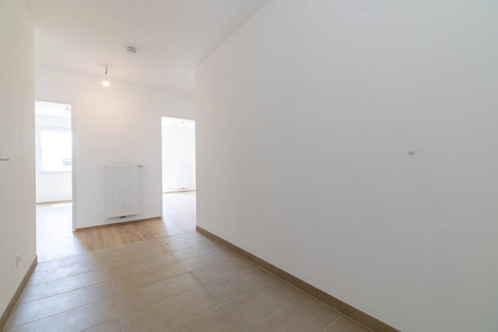 Heller Flur mit Fliesenboden, der in einen Raum mit Holzfußboden übergeht.