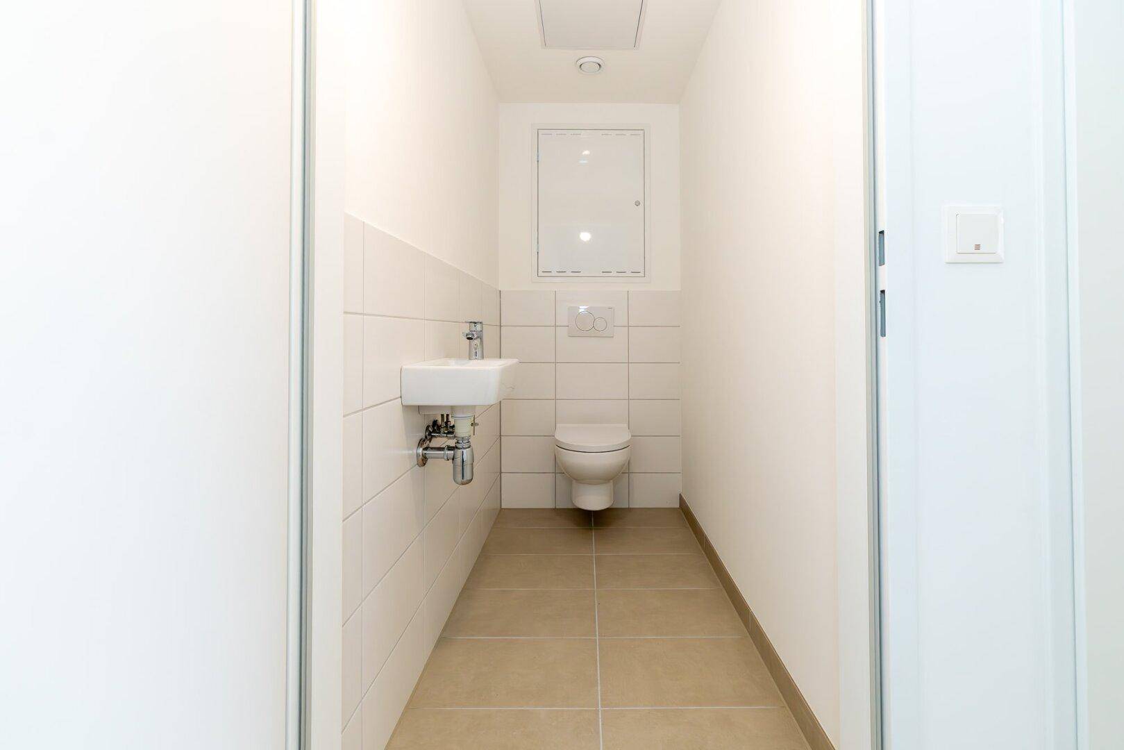 Modernes Gäste-WC mit wandhängendem WC, kleinem Waschbecken und weißen Fliesen.