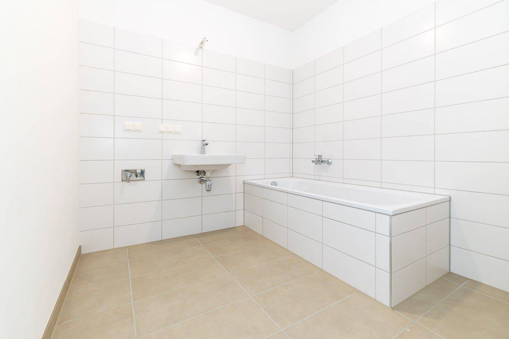 Helles Badezimmer mit Badewanne, Waschbecken und weißen Wandfliesen, bereit zur Gestaltung.