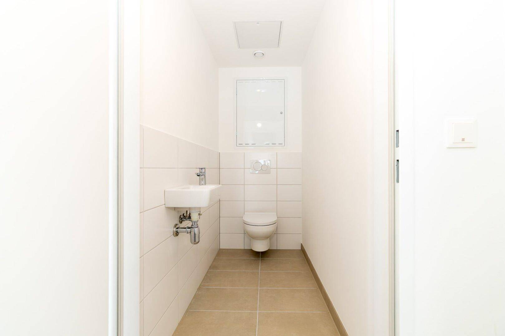 Modernes Gäste-WC mit Wand-WC, kleinem Waschbecken und hellen Fliesen.