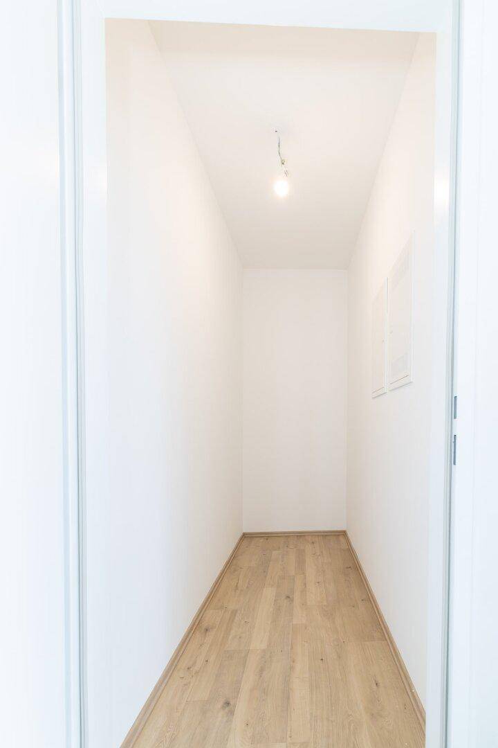 Schmaler, heller Flur mit Laminatboden und weißen Wänden, der zu weiteren Räumen führt.