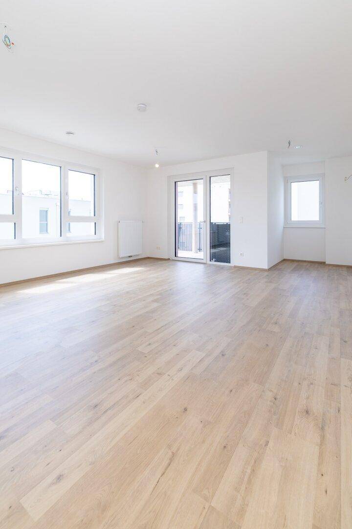 Geräumiger, heller Wohnbereich mit Laminatboden und Zugang zu einem Balkon.