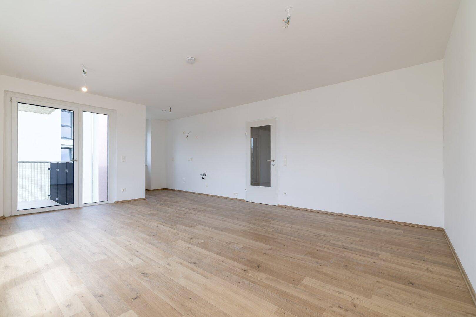 Großer, heller Wohnbereich mit Laminatboden und Schiebetür zum Außenbereich.