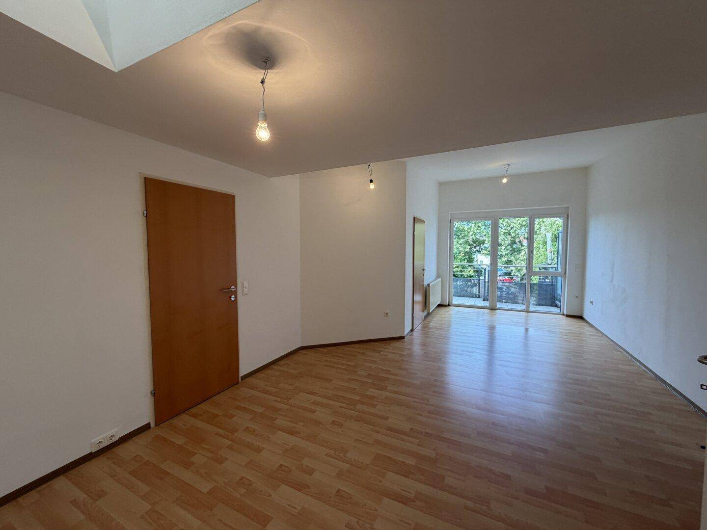 Heller Wohnraum mit Laminatboden und Zugang zu einem Balkon, bereit zur individuellen Gestaltung.