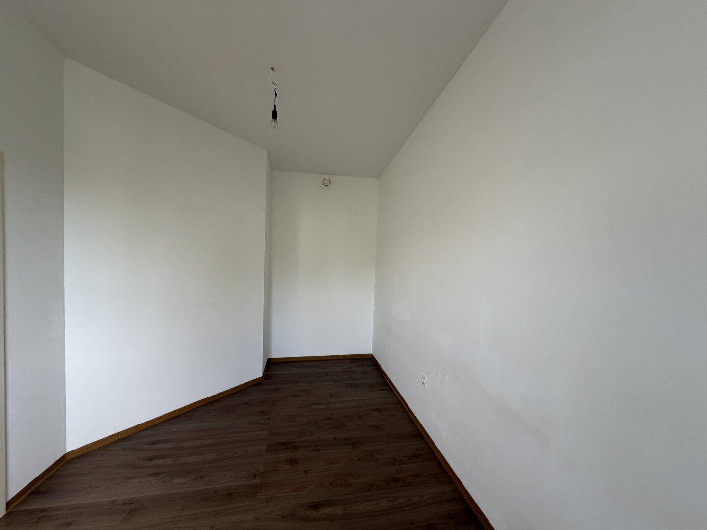 Leerer Raum mit dunklem Laminatboden und weißen Wänden, vielseitig nutzbar.