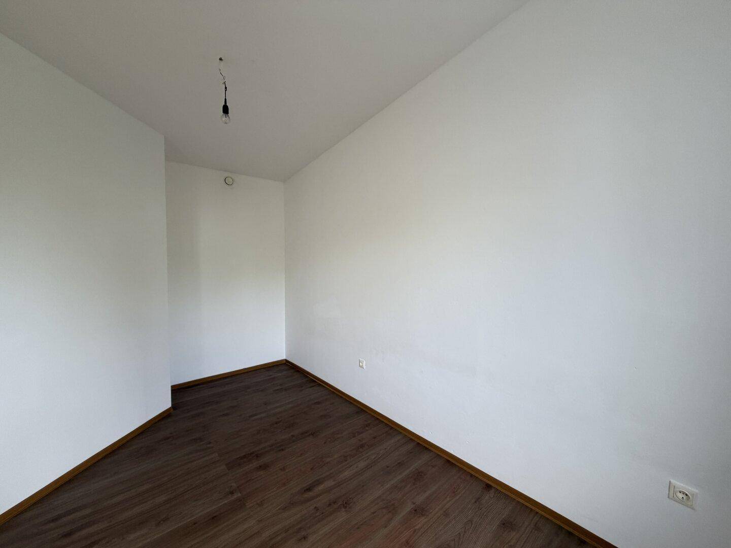 Leerer Raum mit dunklem Laminatboden und weißen Wänden, bietet flexible Nutzungsmöglichkeiten.