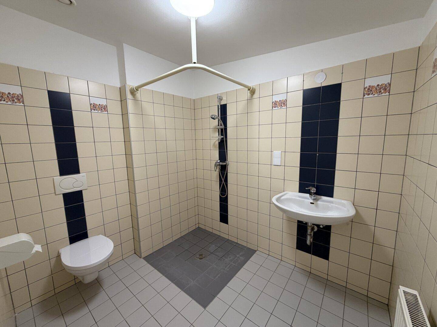 Funktionales Badezimmer mit beigen und dunkelblauen Fliesen, WC, Waschbecken und Duschbereich.