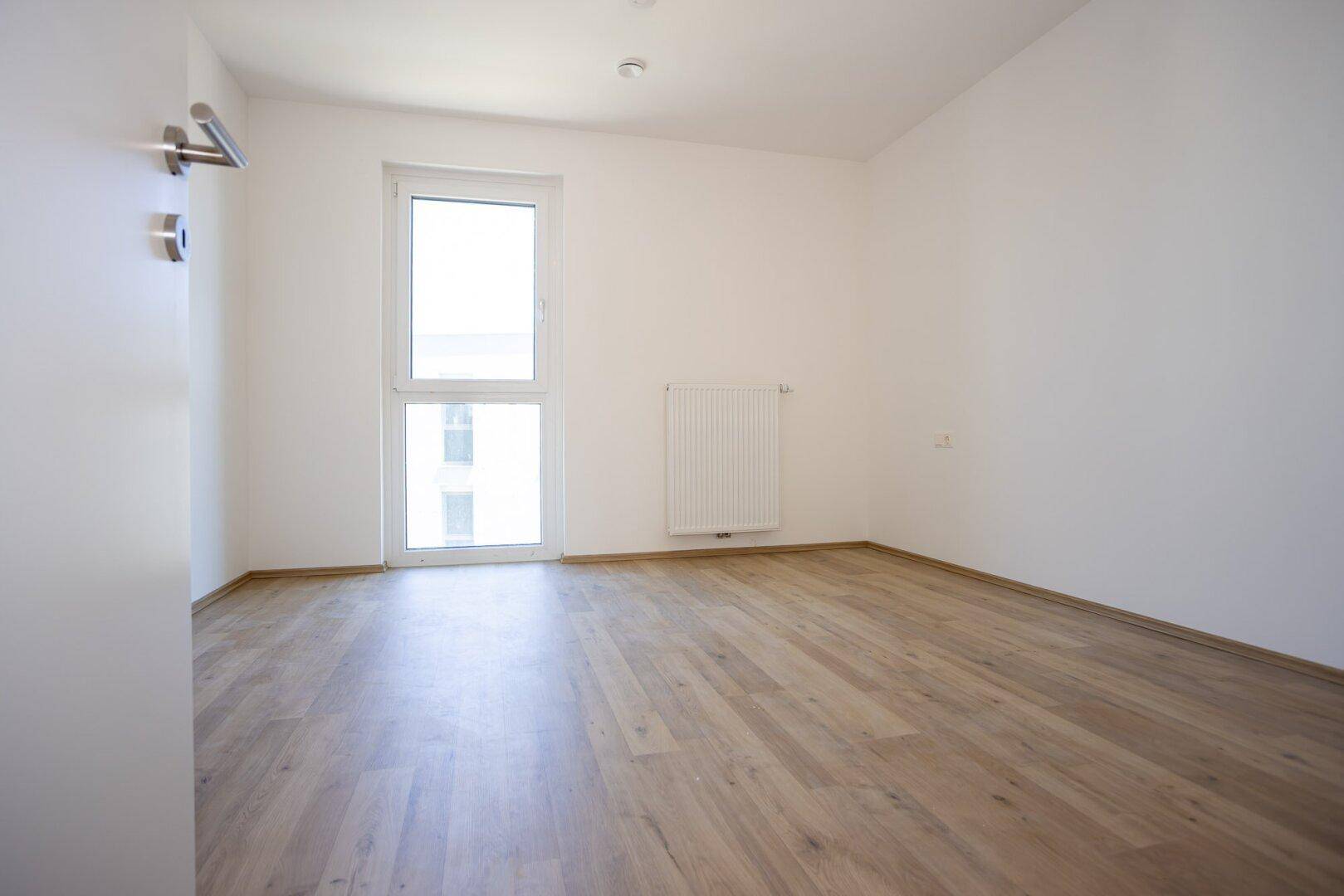 Helles Zimmer mit Laminatboden und Fenster, ideal als Schlaf- oder Arbeitszimmer.