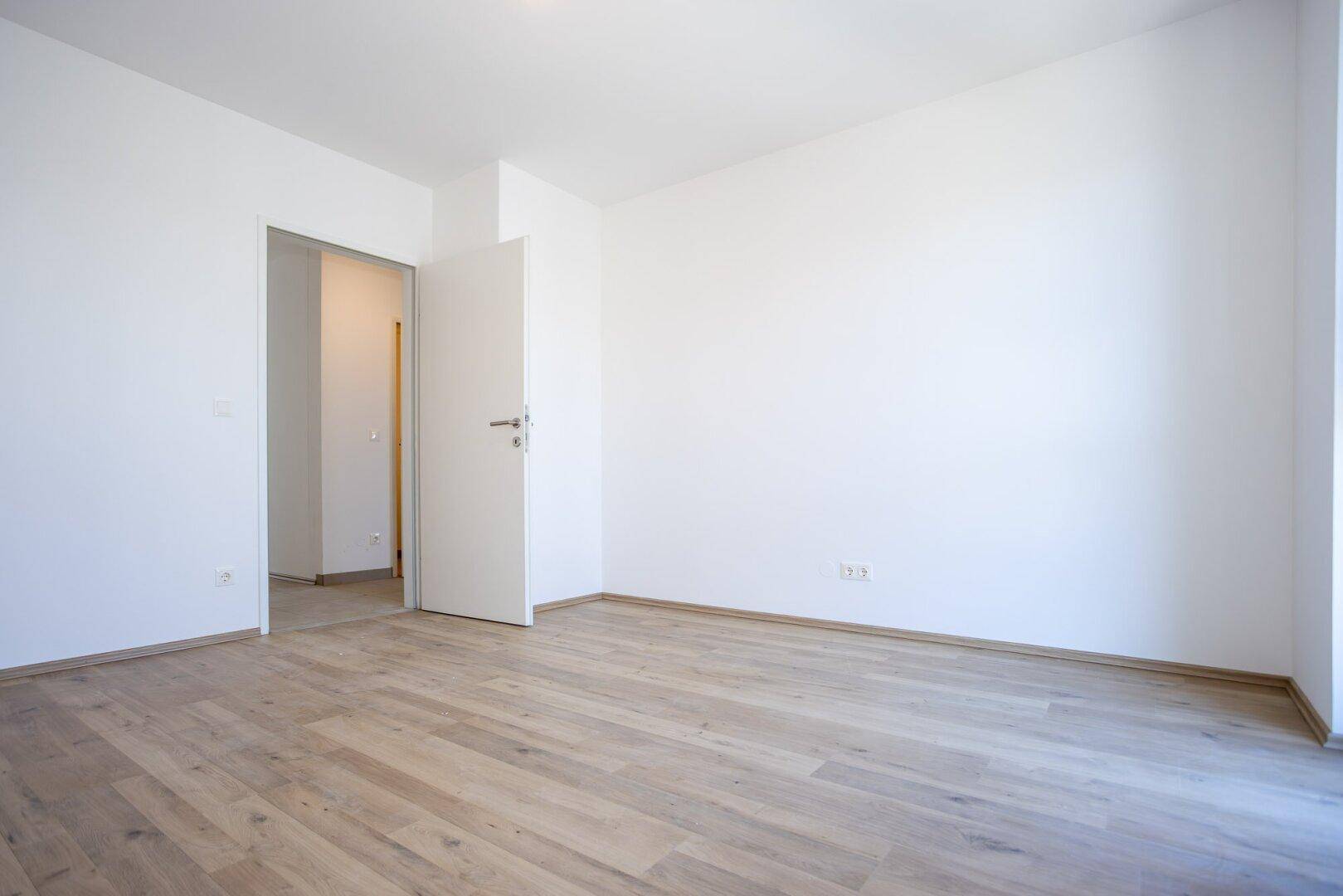 Leeres Zimmer mit Laminatboden und weiß gestrichenen Wänden, bereit zum Einzug.