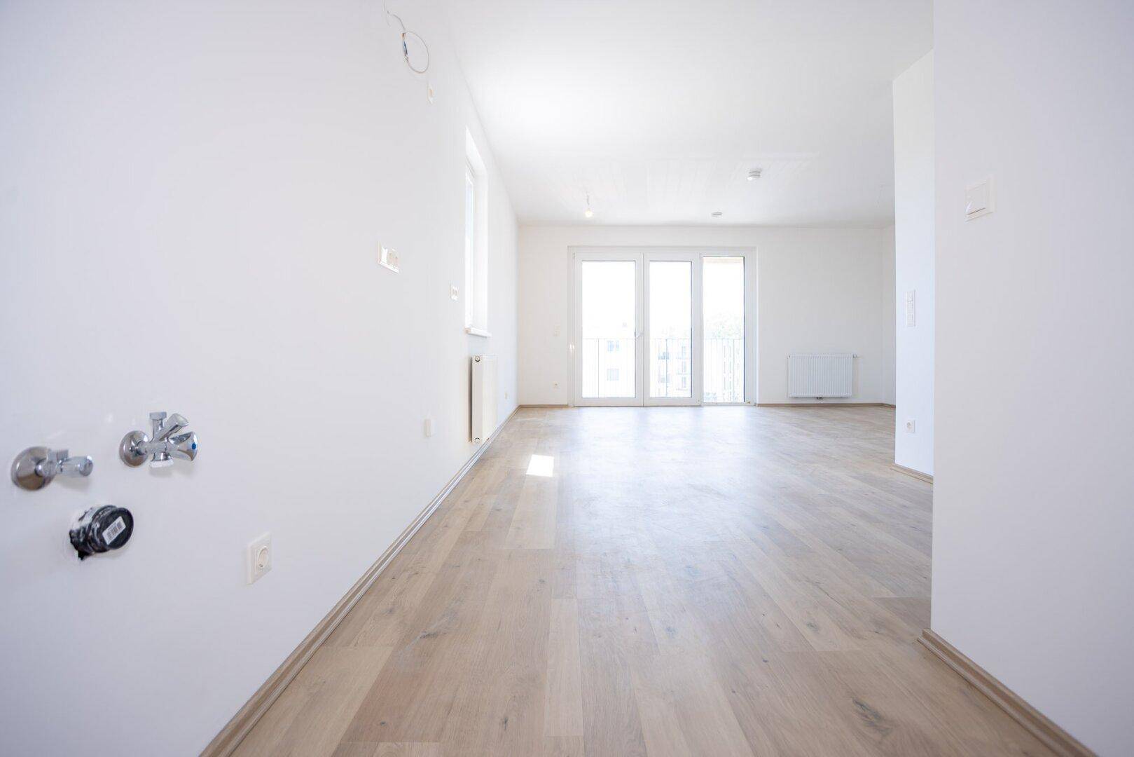 Heller, leerer Wohnraum mit Laminatboden und Zugang zu einem Balkon.