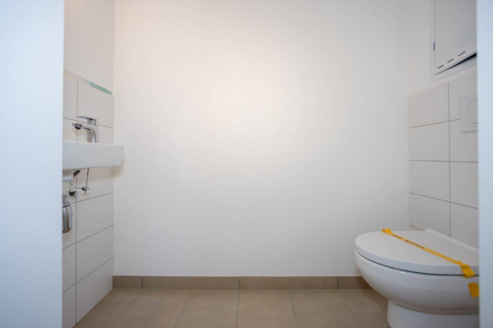 Separates Gäste-WC mit Toilette, kleinem Waschbecken und weißen Fliesen.