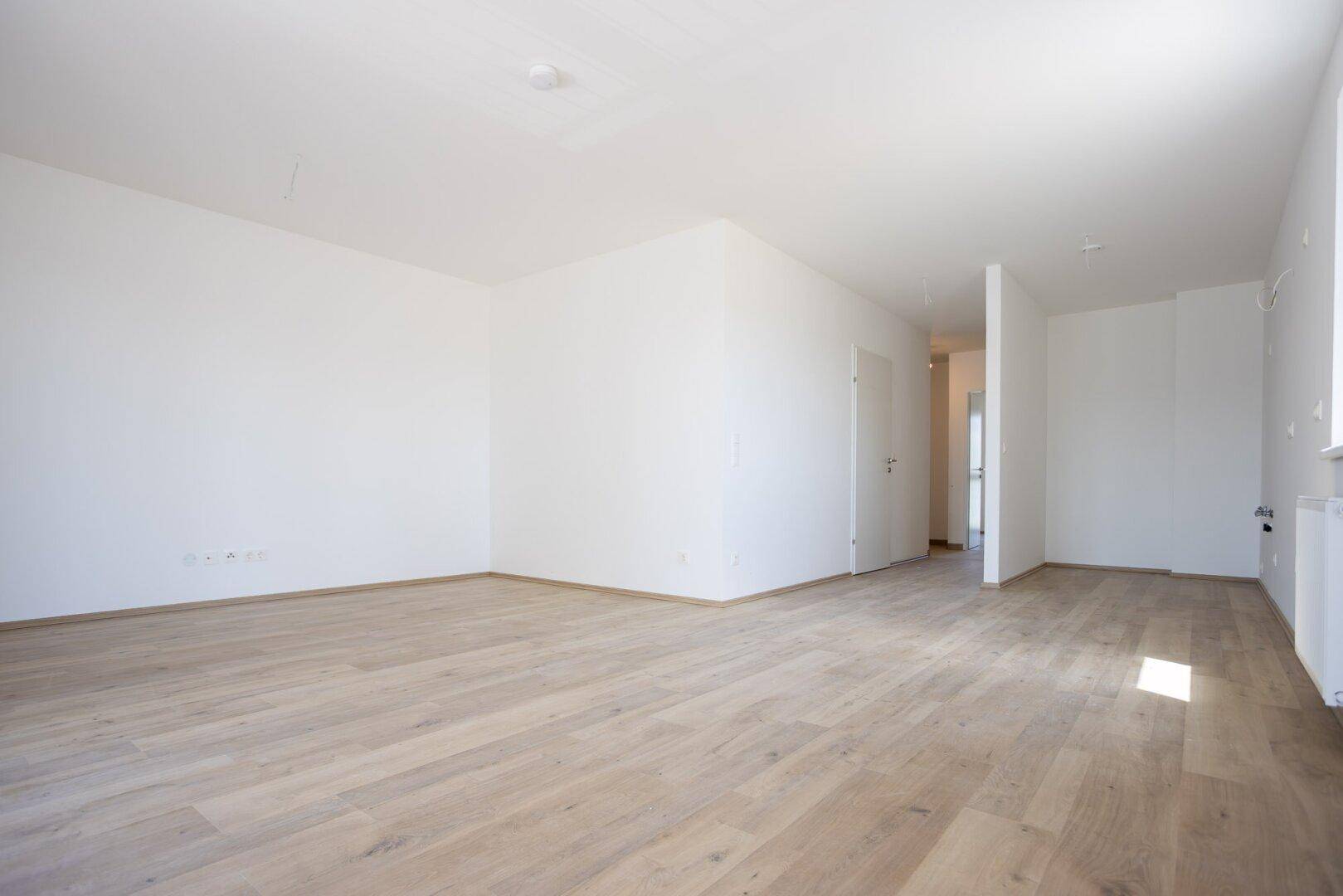 Geräumiger, heller Wohnbereich mit Laminatboden und weiß gestrichenen Wänden.
