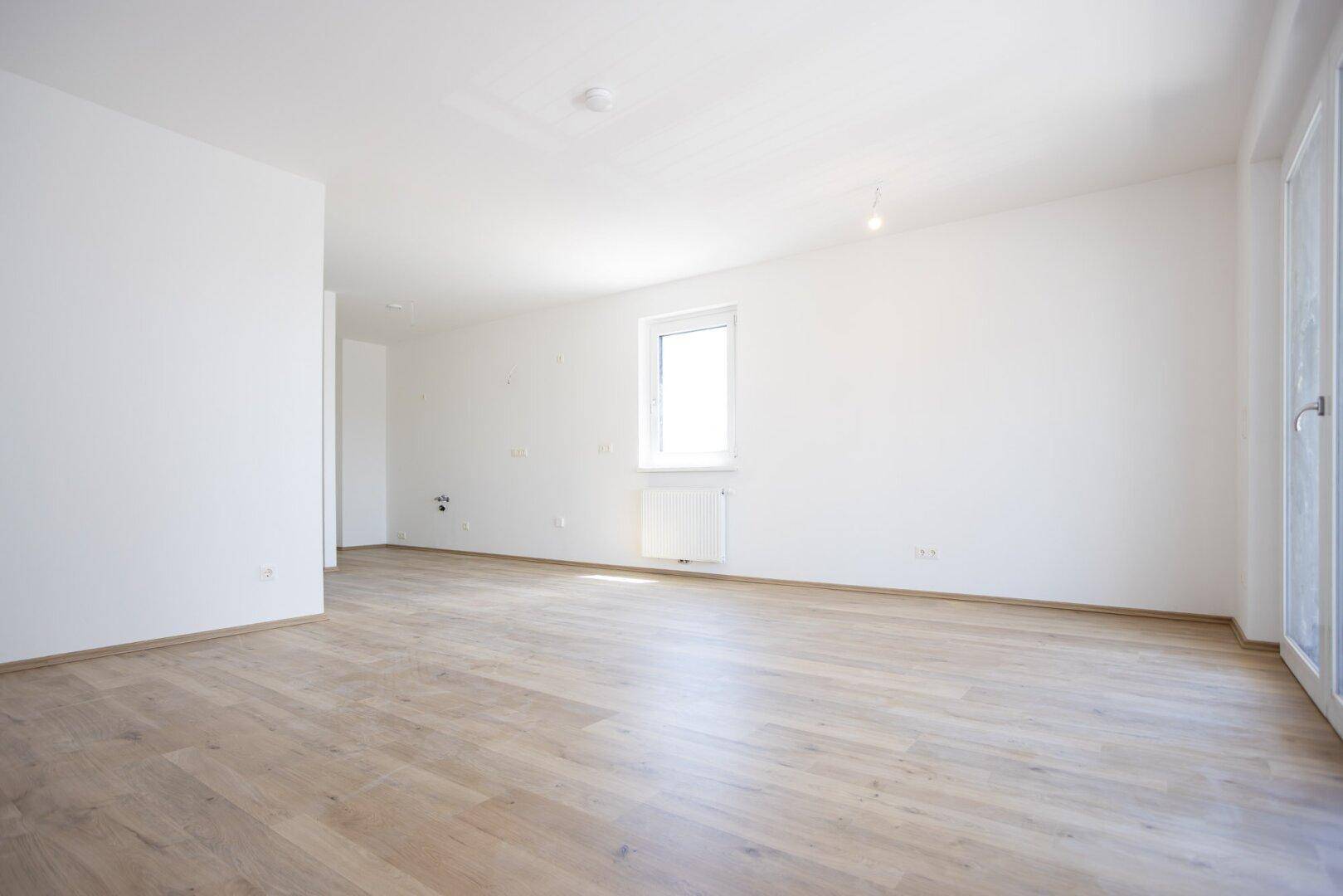 Heller Wohnraum mit Laminatboden und einem Fenster, das viel Tageslicht hereinlässt.