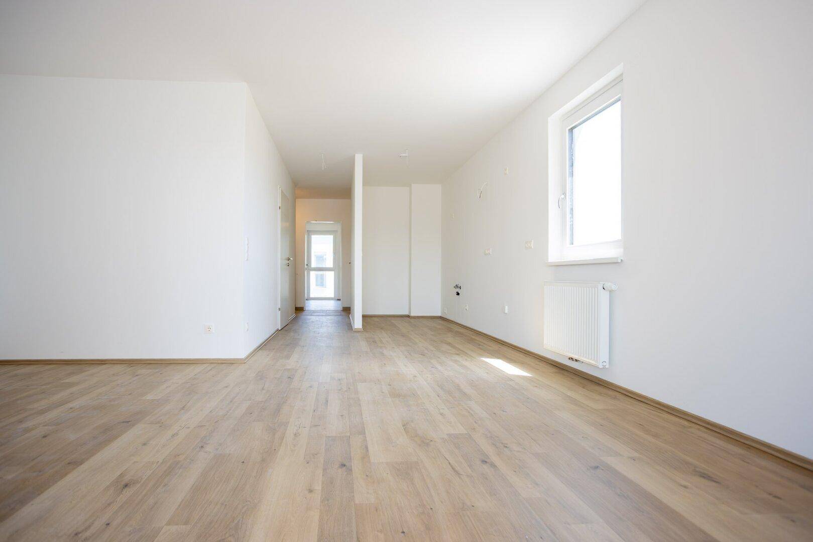 Offener Wohnbereich mit Laminatboden und viel Tageslicht, ideal für individuelle Gestaltung.
