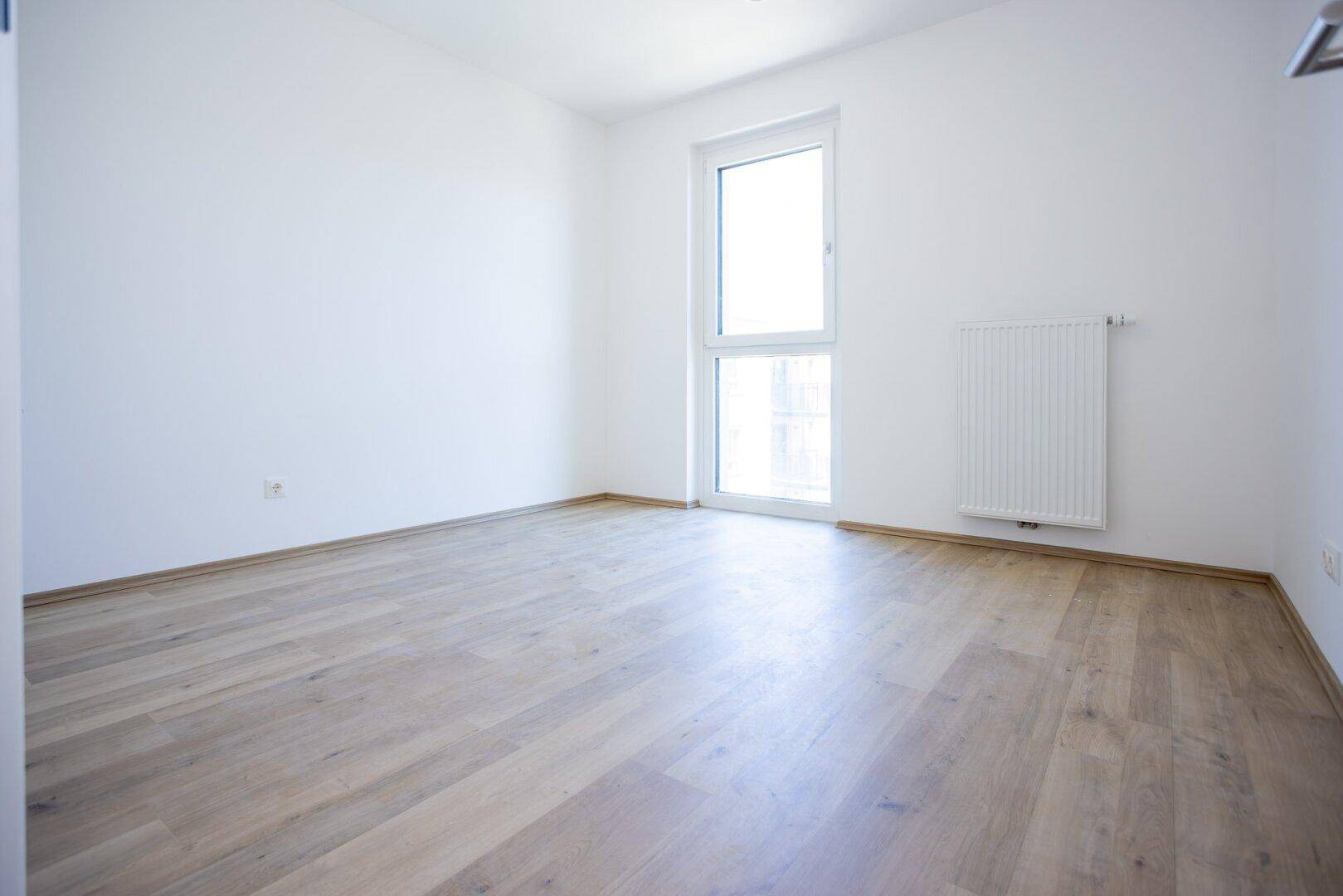 Helles Zimmer mit Laminatboden und großem Fenster, geeignet als Schlaf- oder Kinderzimmer.