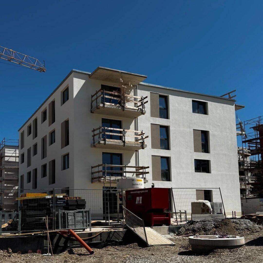 Neubau eines Mehrfamilienhauses mit Balkonen auf einer Baustelle unter blauem Himmel.