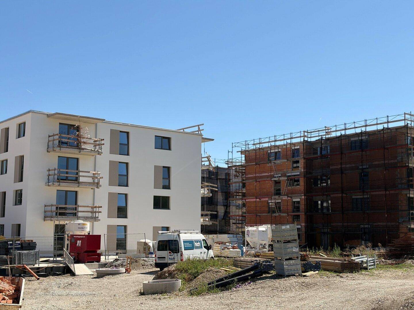 Zwei Neubauten auf einer Baustelle, einer mit weißer Fassade und der andere im Rohbau.