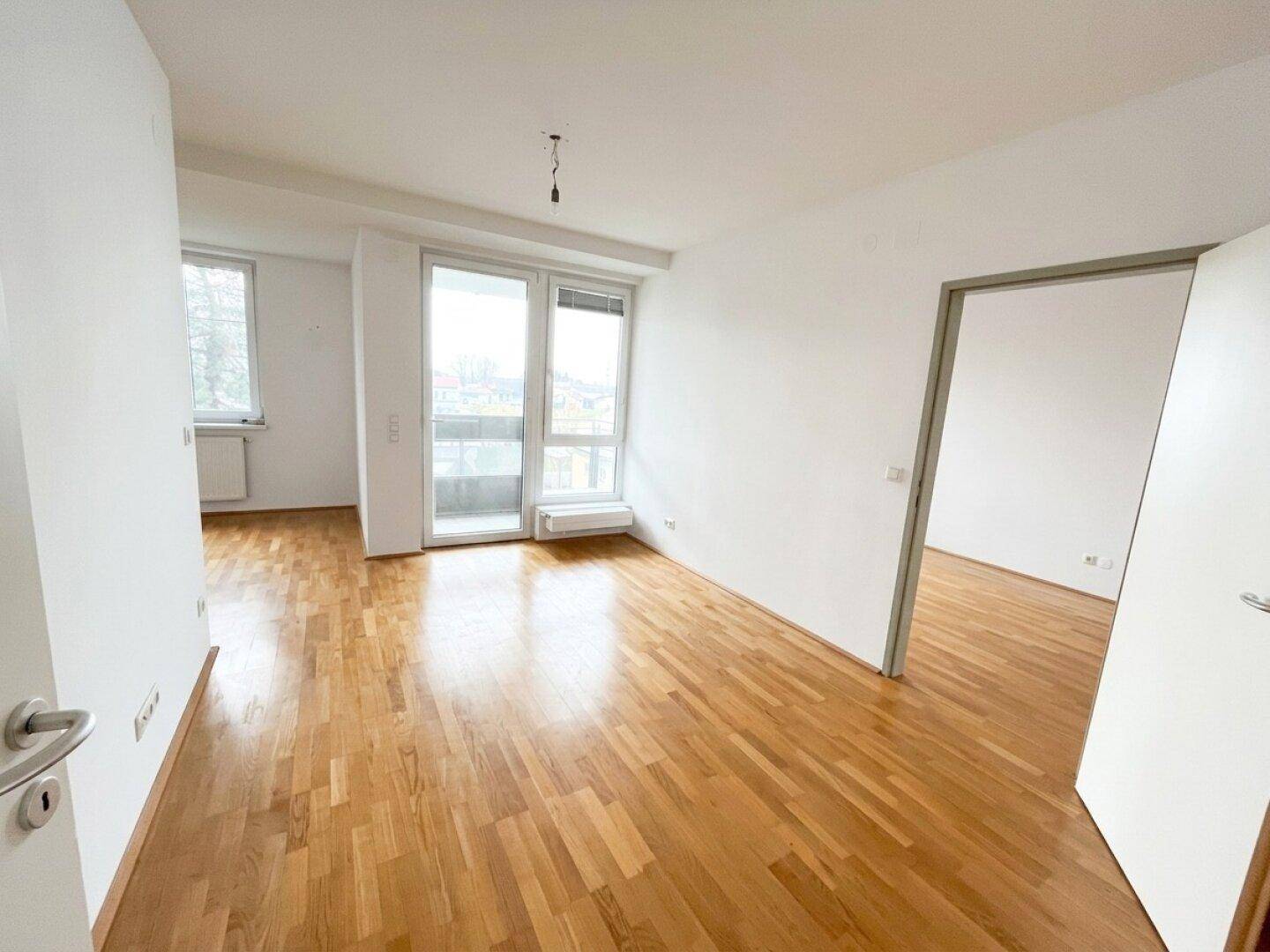 Heller Wohnbereich mit Parkettboden und Zugang zu einem Balkon, der viel natürliches Licht bietet.