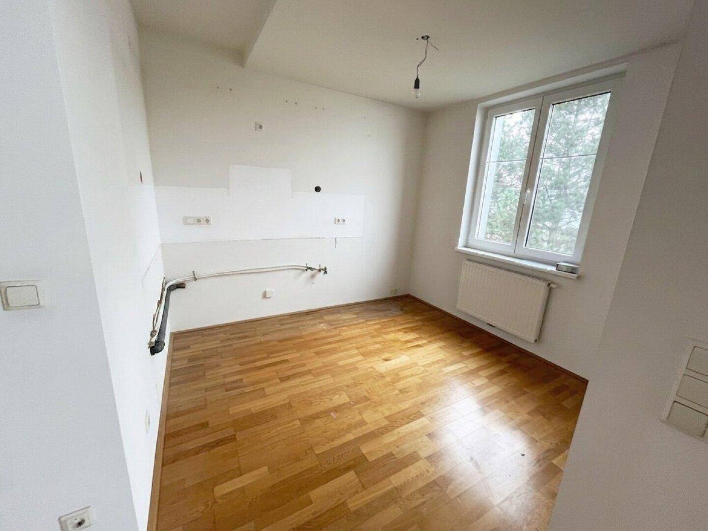 Leerer Küchenraum mit Parkettboden und Fenster, vorbereitet für die Installation einer Einbauküche.