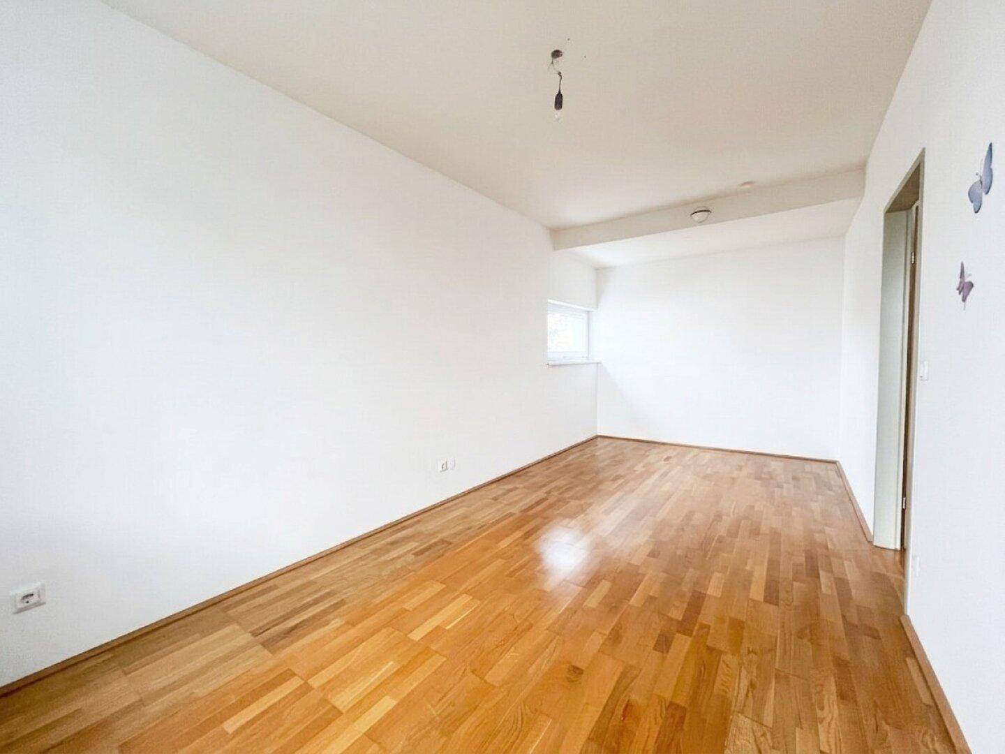 Helles Schlafzimmer mit Parkettboden und einem kleinen Fenster, das für natürliche Belüftung sorgt.