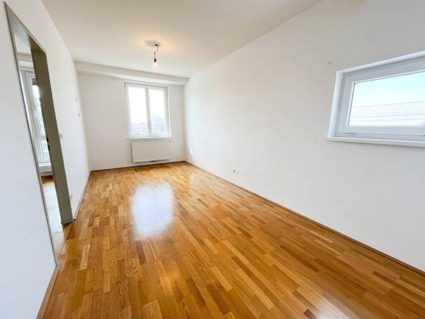 Geräumiges Schlafzimmer mit Parkettboden und zwei Fenstern, die für ausreichend Tageslicht sorgen.