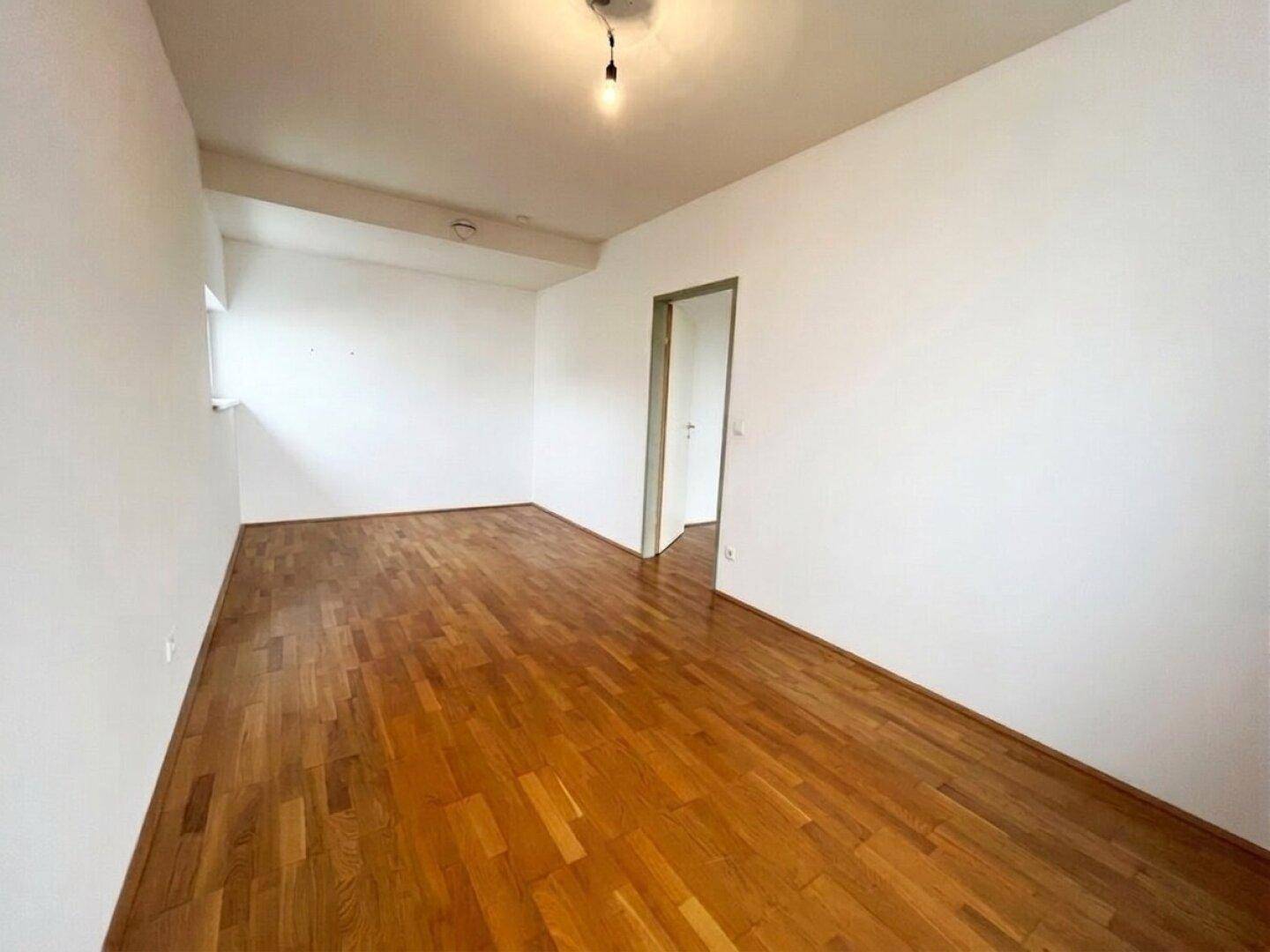 Leeres Zimmer mit glänzendem Parkettboden und weißen Wänden, bereit zur individuellen Gestaltung.