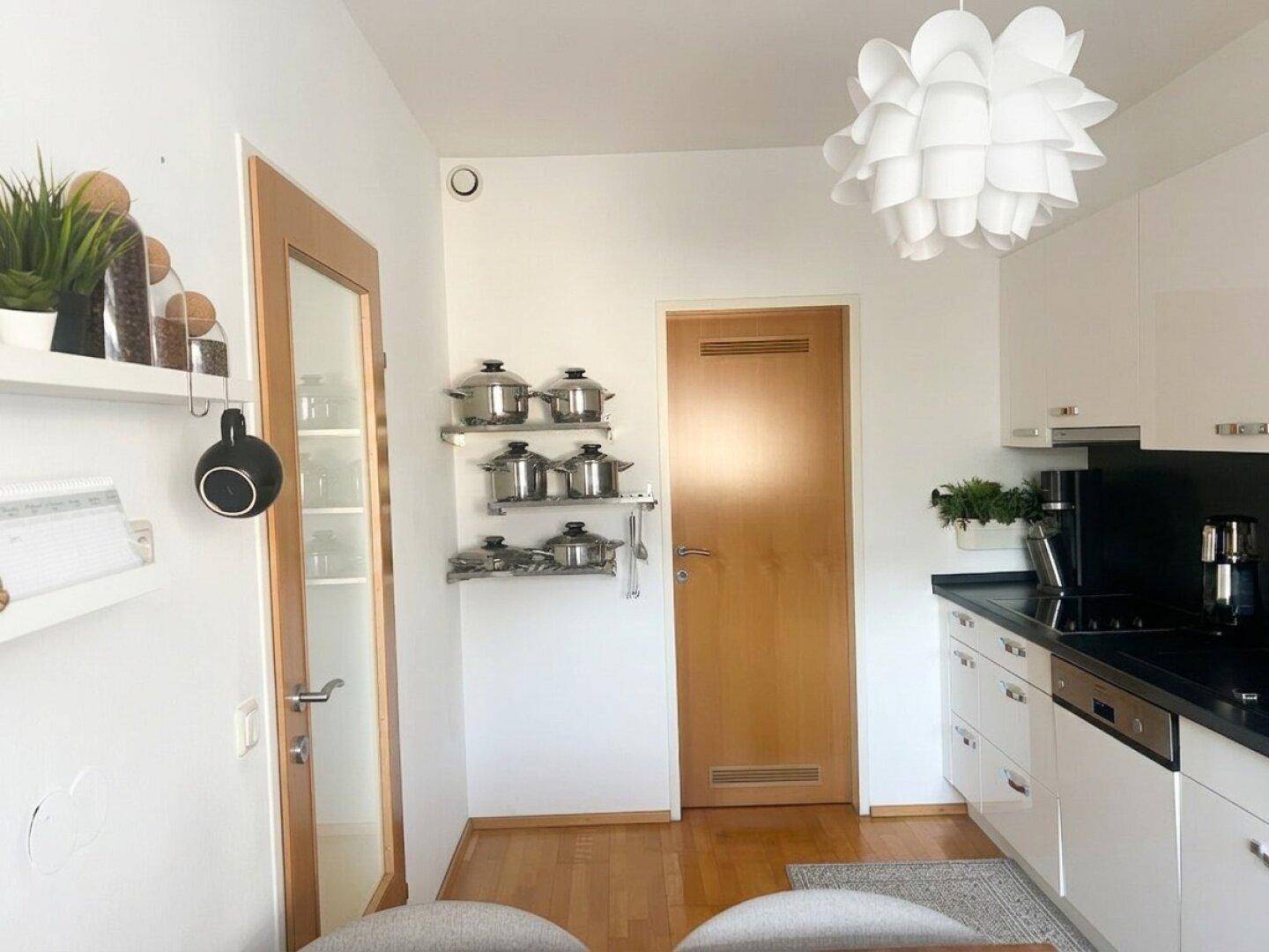 Blick auf den Essbereich der Küche mit Holztür, Wandregalen für Kochutensilien und Parkettboden.