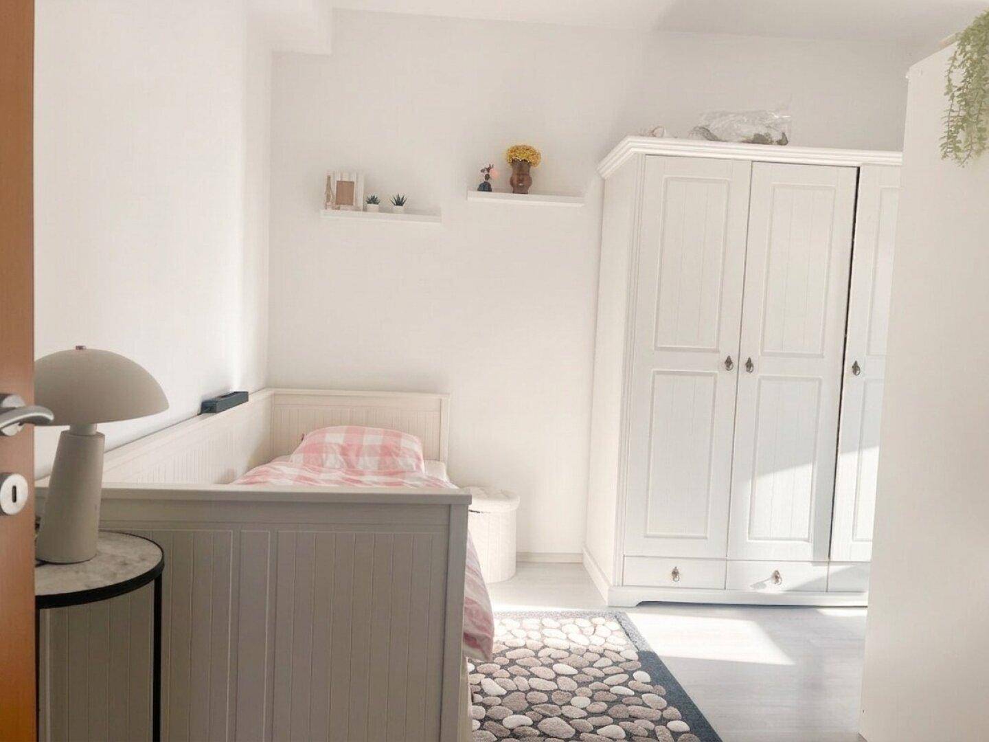 Freundliches Kinder- oder Gästezimmer mit weißem Bett und Schrank, gut beleuchtet durch Tageslicht.