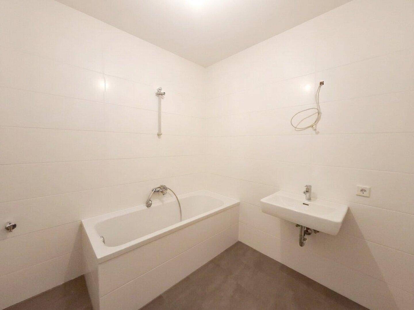Modernes Badezimmer mit weißen Fliesen, einer Badewanne und einem wandmontierten Waschbecken.