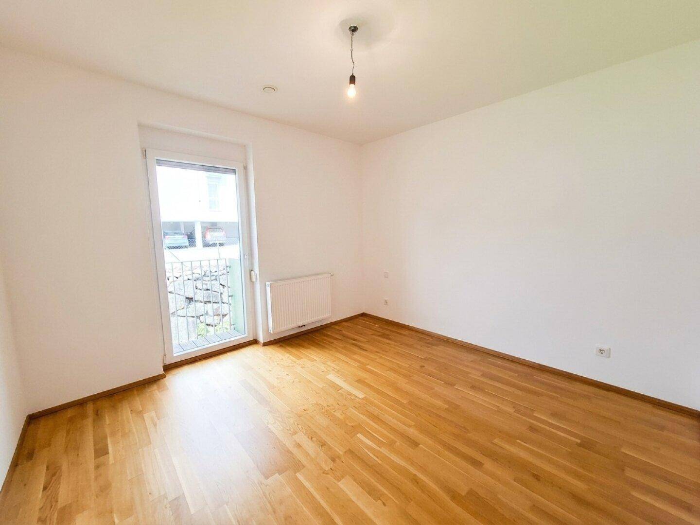 Helles Schlafzimmer mit Parkettboden und Zugang zu einem kleinen Balkon, ideal für frische Luft.