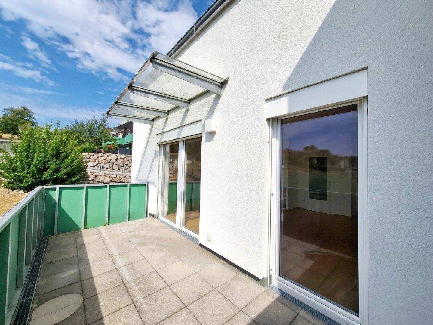 Heller Balkon mit Fliesenboden, Glasüberdachung und Zugang zu den Innenräumen durch große Fenstertüren.