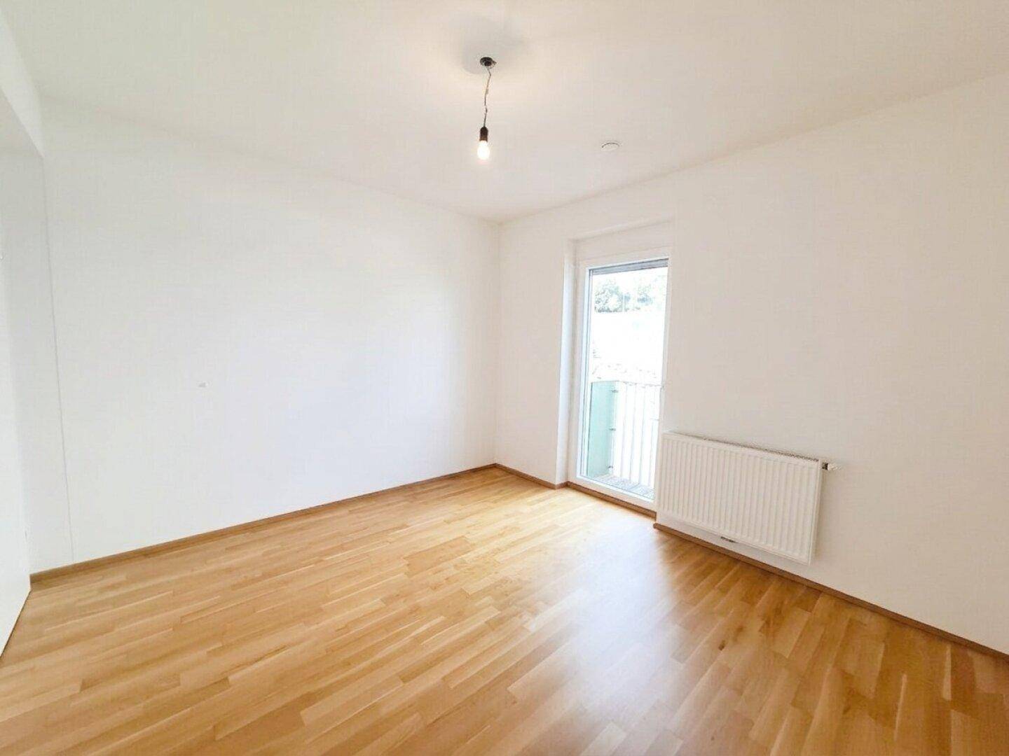 Geräumiges Schlafzimmer mit Holzfußboden und weiß gestrichenen Wänden, bietet direkten Zugang ins Freie.
