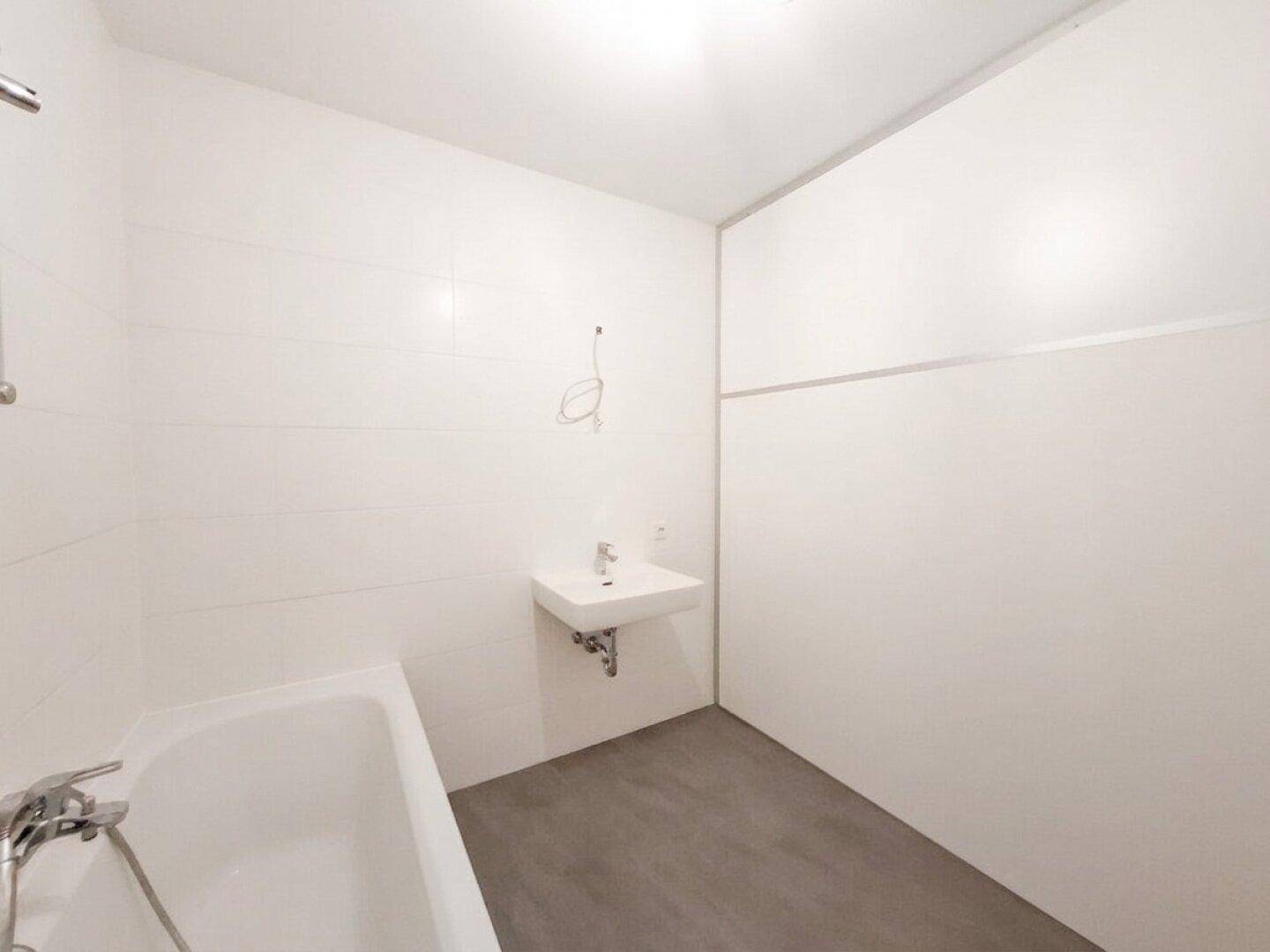 Funktionales Badezimmer mit Badewanne und wandhängendem Waschbecken, ausgestattet mit hellen Wandfliesen.