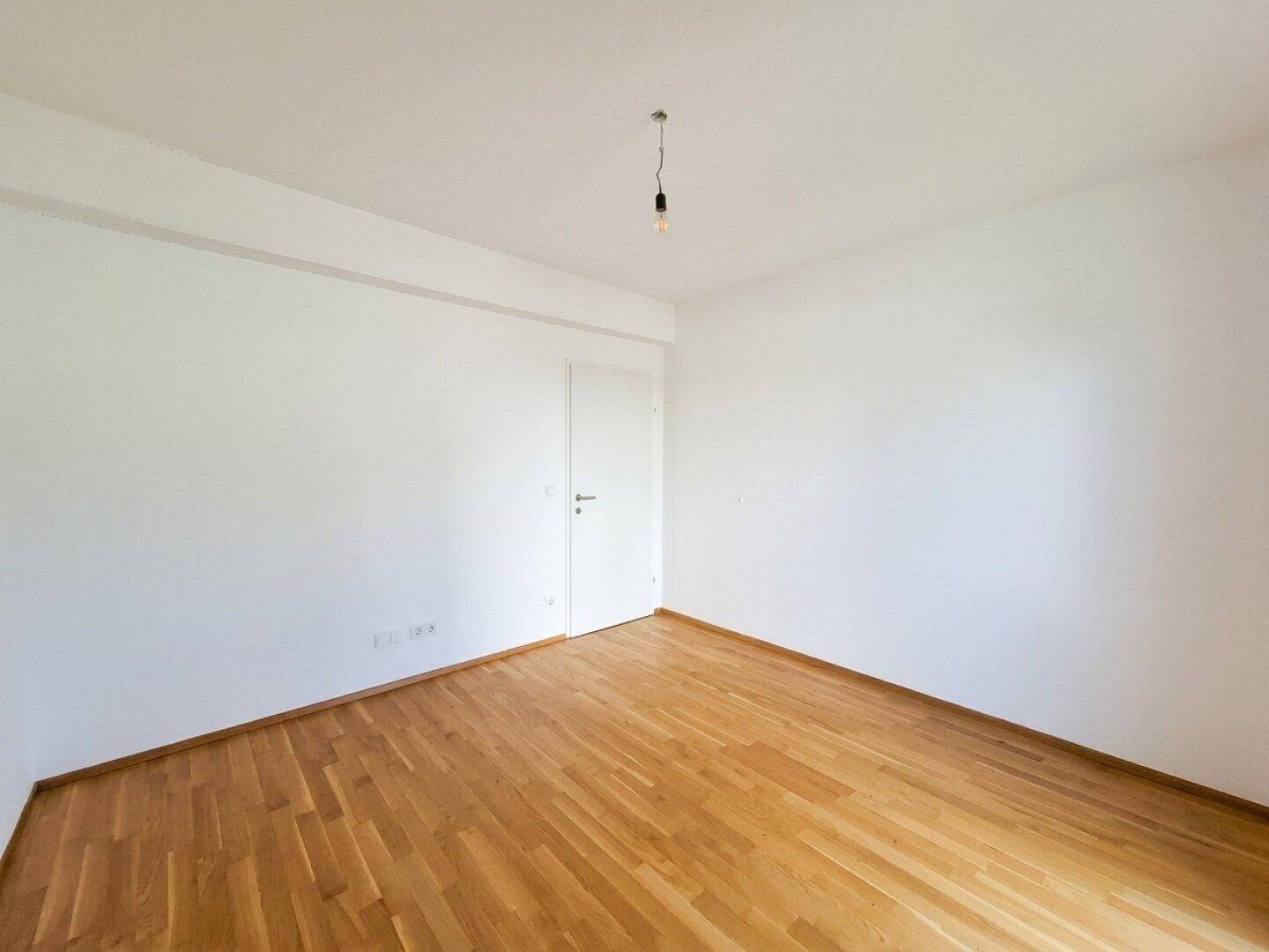 Leeres Zimmer mit hellem Parkettboden und weißen Wänden, vielseitig nutzbar als Schlaf- oder Arbeitszimmer.