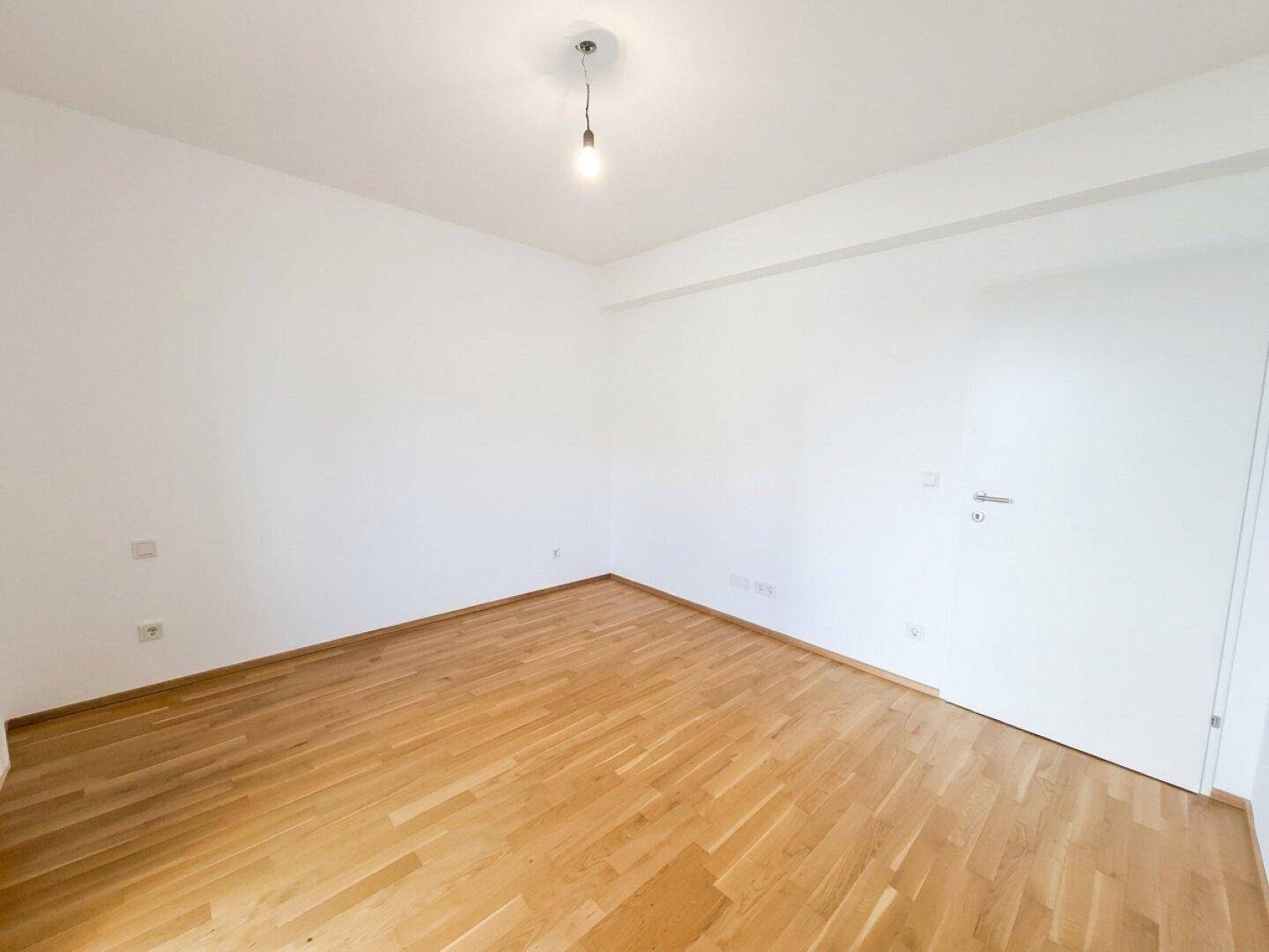 Helles Zimmer mit Parkettboden und schlichten weißen Wänden, bietet eine neutrale Basis für individuelle Einrichtung.