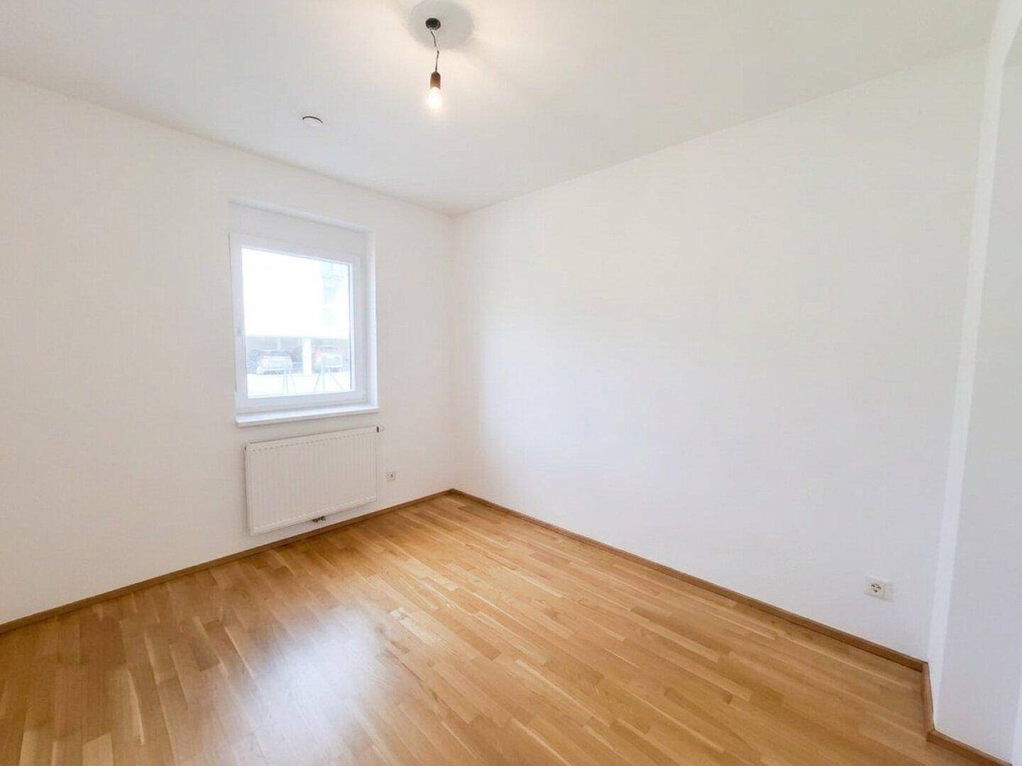 Freundliches Zimmer mit Parkettboden und Fenster, das viel Tageslicht hereinlässt.