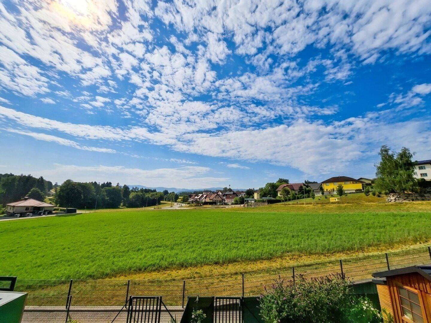 Weitläufiger Blick über grüne Felder und die umliegende Landschaft unter einem strahlend blauen Himmel.