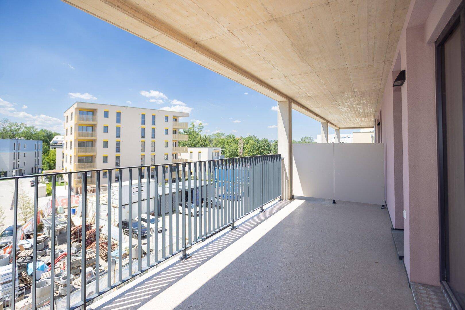 Langer Balkon eines Neubaus mit Blick auf umliegende Gebäude und eine Baustelle unter blauem Himmel.