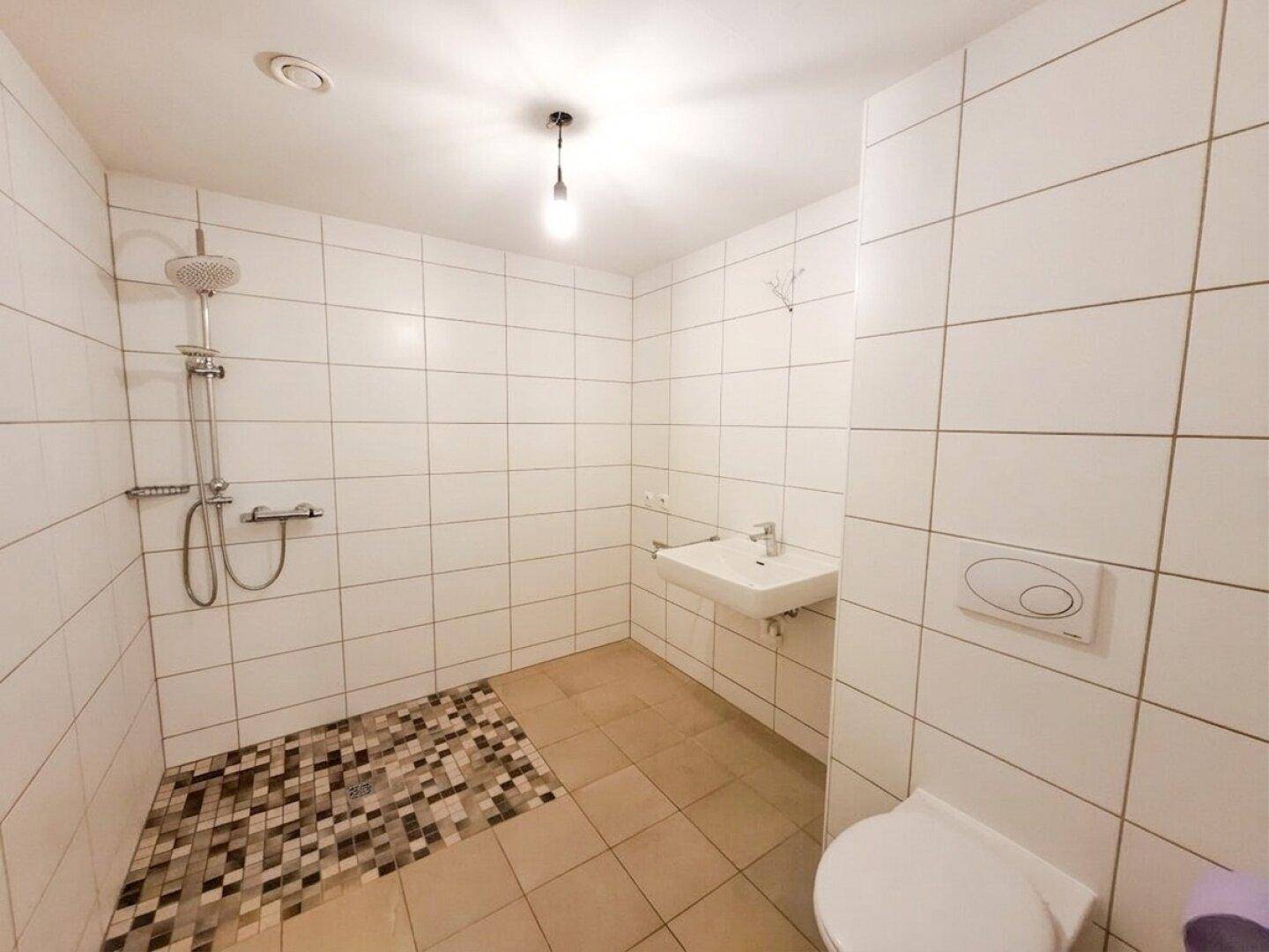 Modernes Badezimmer mit weißen Fliesen, ebenerdiger Dusche, Waschbecken und Wand-WC.