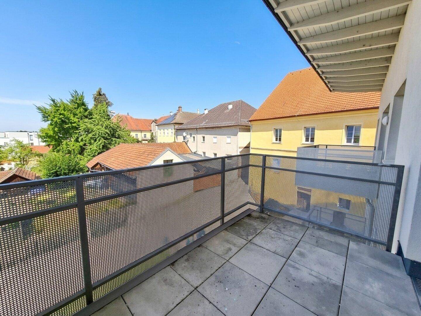 Balkon mit Fliesenboden und Blick auf die Dächer der umliegenden Häuser und Gärten.