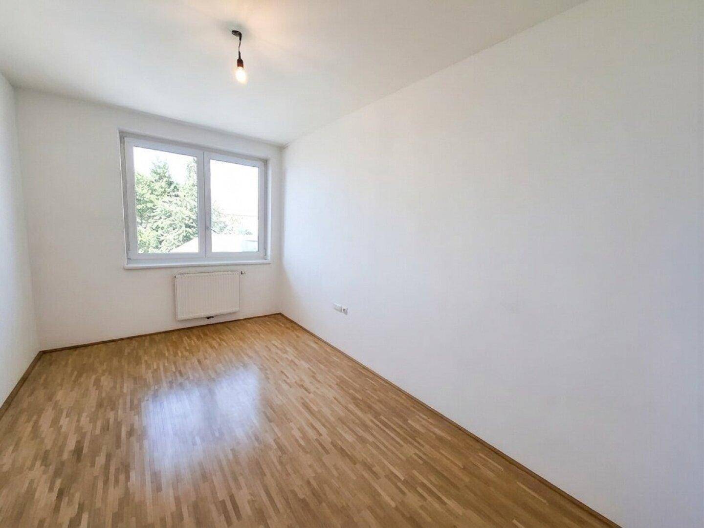 Ruhiges Schlafzimmer mit Parkettboden und einem Fenster, das viel Tageslicht hereinlässt.