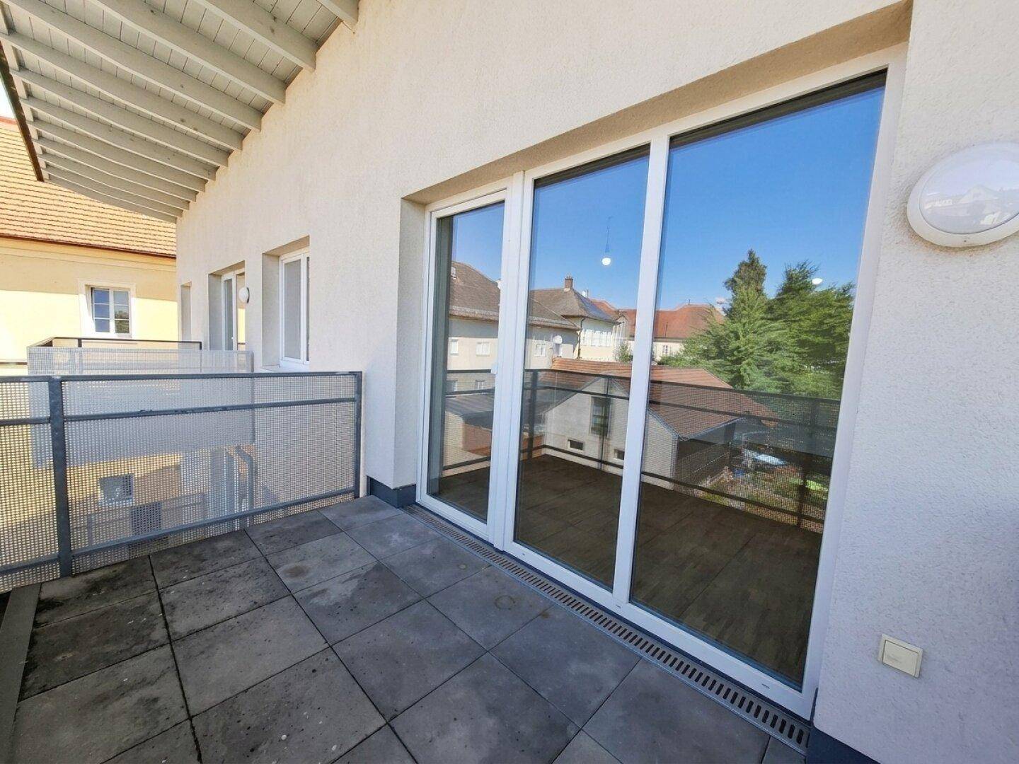 Geräumiger Balkon mit Schiebetüren und Blick auf die angrenzenden Gebäude und Bäume.