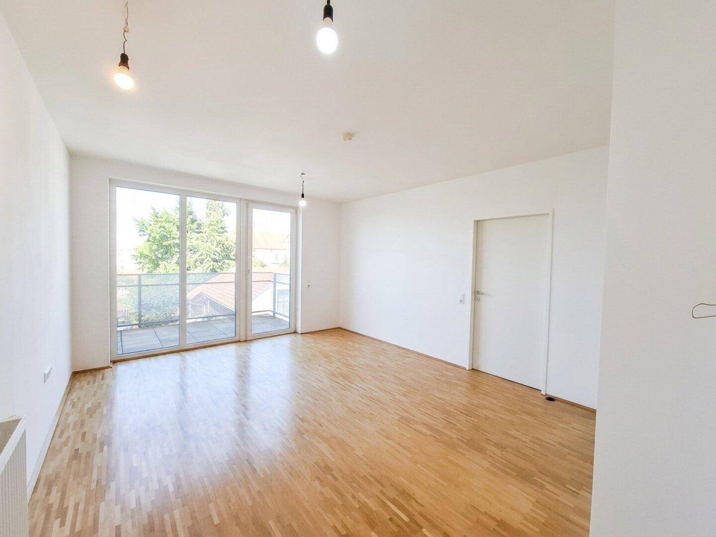 Helles Wohnzimmer mit Parkettboden und großen Fenstertüren, die zum Balkon führen.
