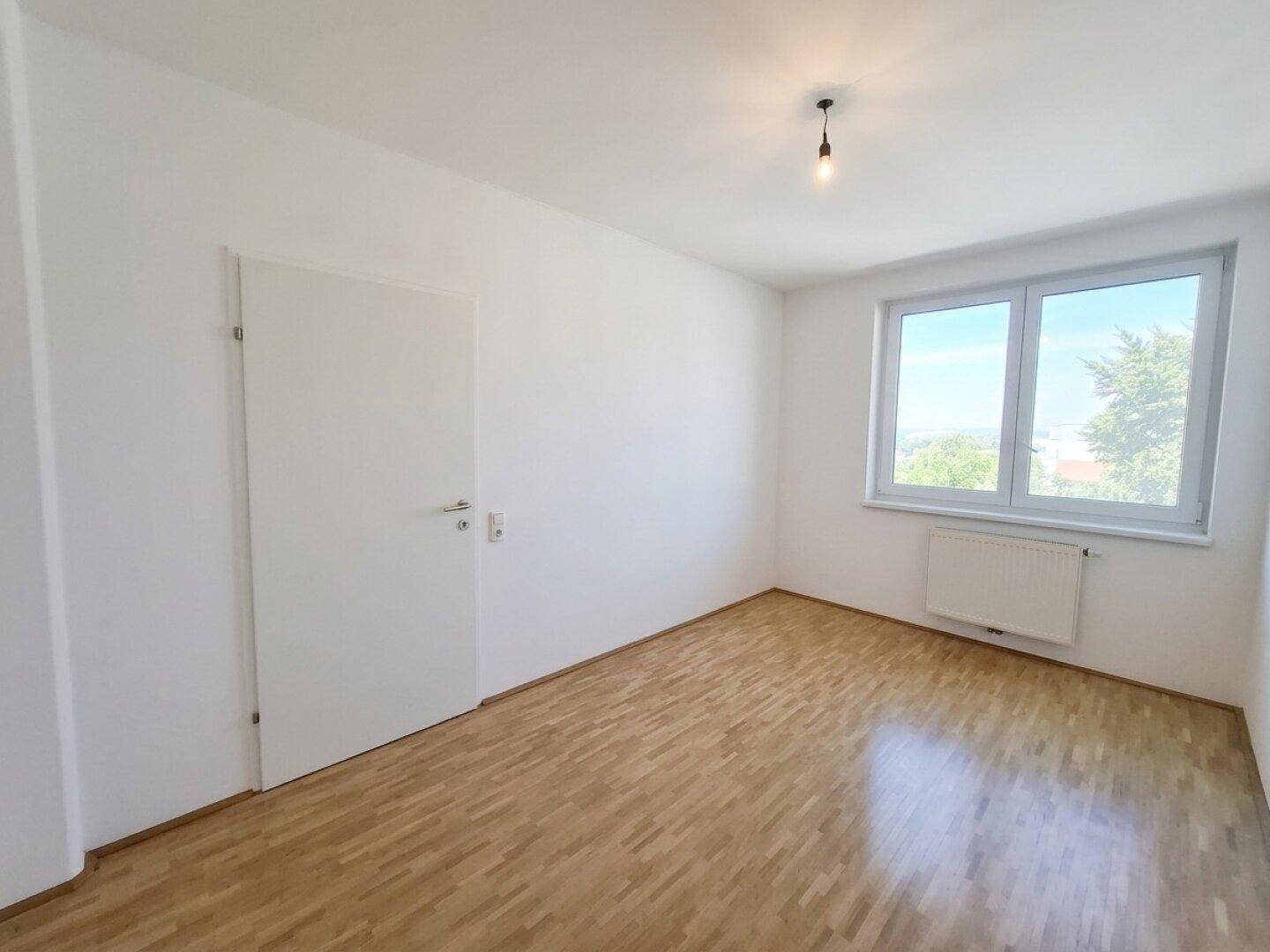 Helles Schlafzimmer mit Holzboden und einem großen Fenster, das einen weiten Ausblick bietet.