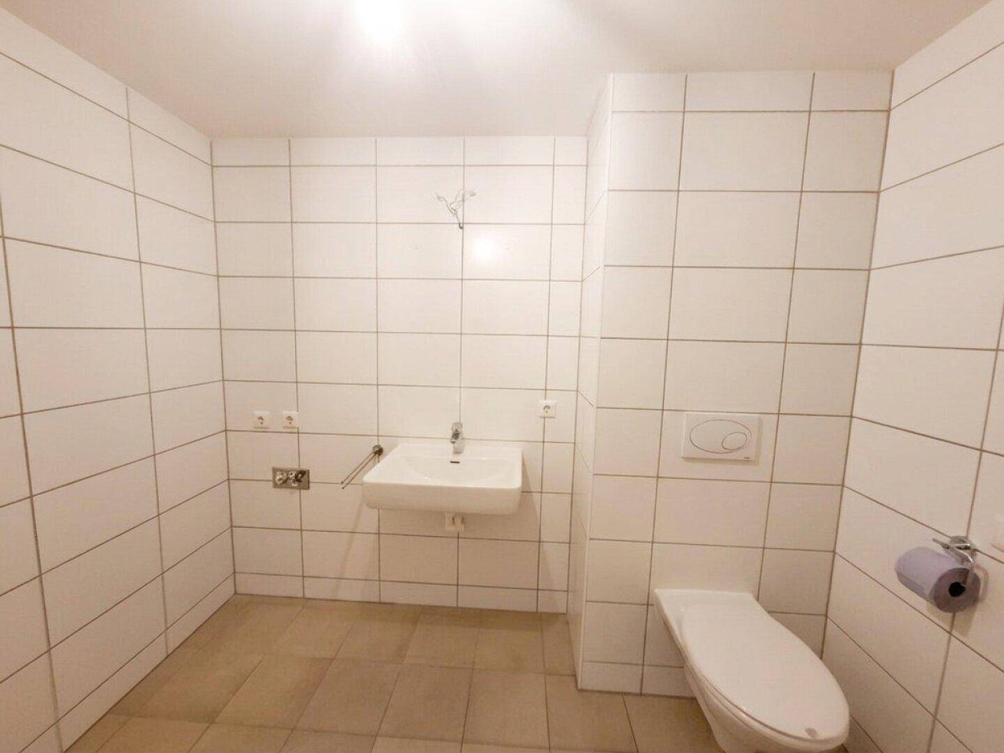 Sauber gefliestes Badezimmer mit Waschbecken und Wand-WC, bietet ausreichend Platz.