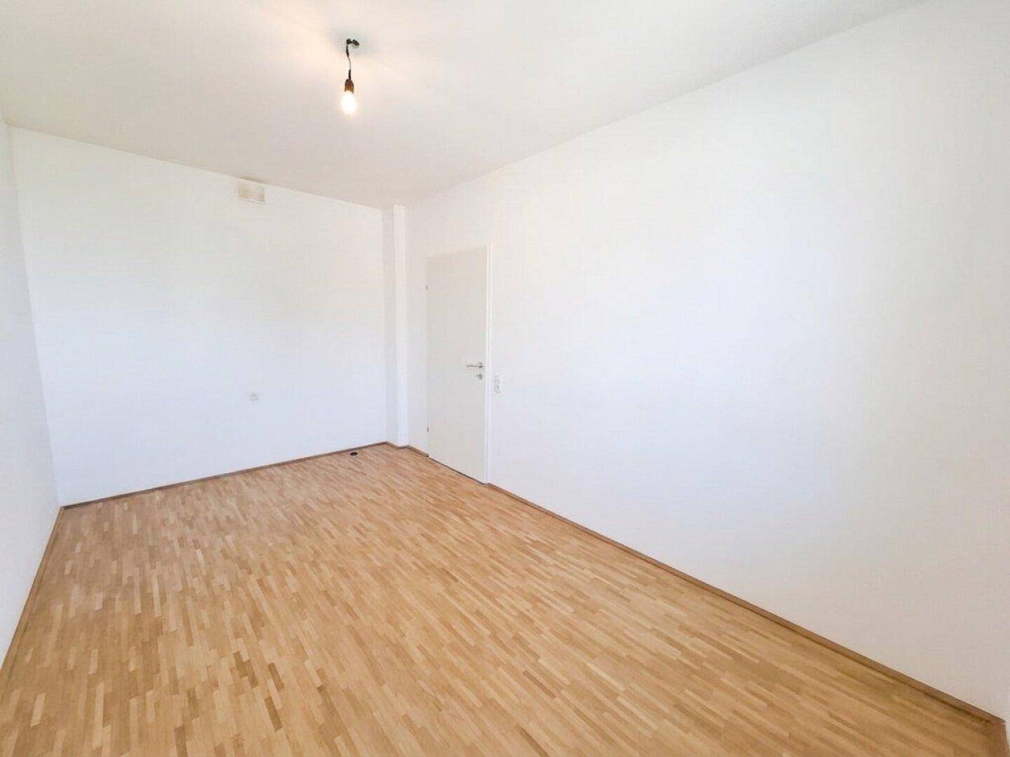 Schlichtes Schlafzimmer mit Parkettboden und weißen Wänden, ideal für eine individuelle Einrichtung.
