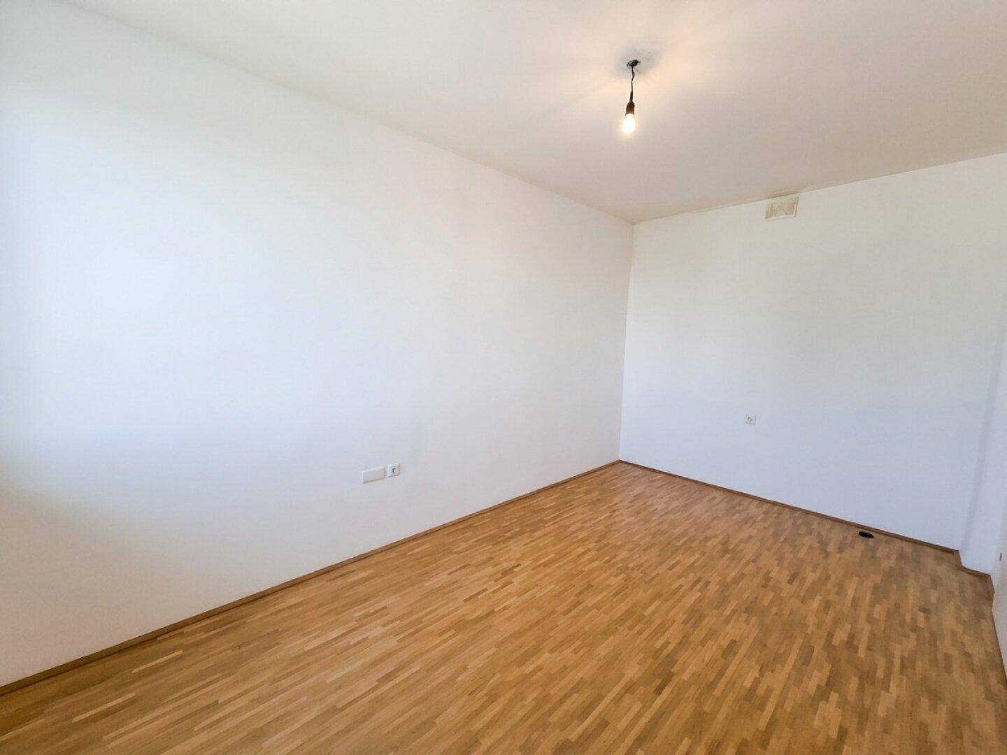 Leeres Zimmer mit hellem Parkettboden und weißen Wänden, bietet vielseitige Nutzungsmöglichkeiten.